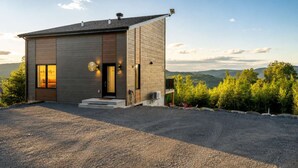 Una casa moderna de dos pisos con entrada para coches, puerta principal y vistas del paisaje circundante.