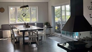 Une cuisine moderne dotée d’une grande table à manger, de chaises, d’un four encastré et offrant une vue sur l’extérieur grâce à de grandes fenêtres.