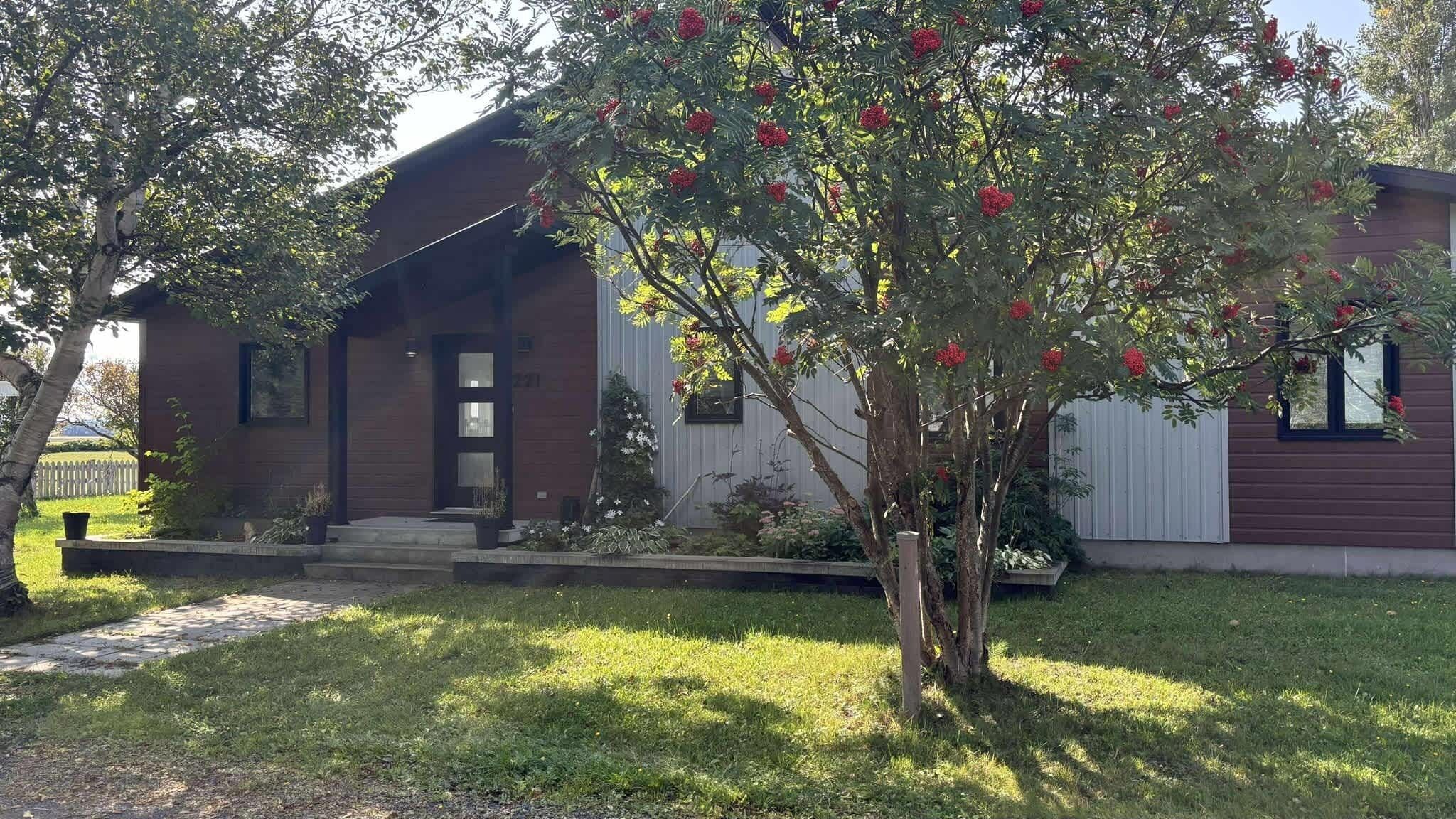 A house with a front porch, a small garden, and a tree with red flowers.