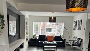 A modern living room with a black leather sofa, a black rug, and a large window with blinds.