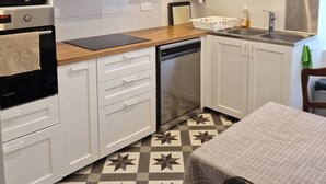 A modern kitchen with white cabinets, a stainless steel range hood, a microwave, an oven, a dishwasher, and a tiled floor with a geometric pattern. - Apartment F3 Villa MonRêve (La Bourboule)