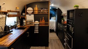 A compact kitchen with a coffee machine, a cutting board, and a microwave.