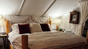 Um quarto com tenda, uma cama de madeira, uma mesinha de cabeceira, uma luminária e um quadro pendurado.