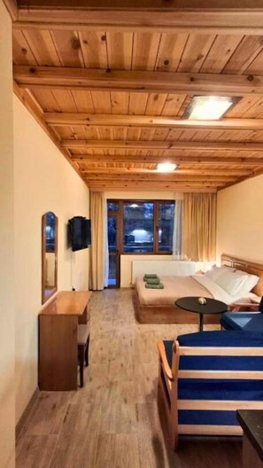 Ein Hotelzimmer mit Holzboden, einem Bett, einem Schreibtisch, einem Stuhl, einem kleinen Tisch und einem fenster mit Vorhängen.