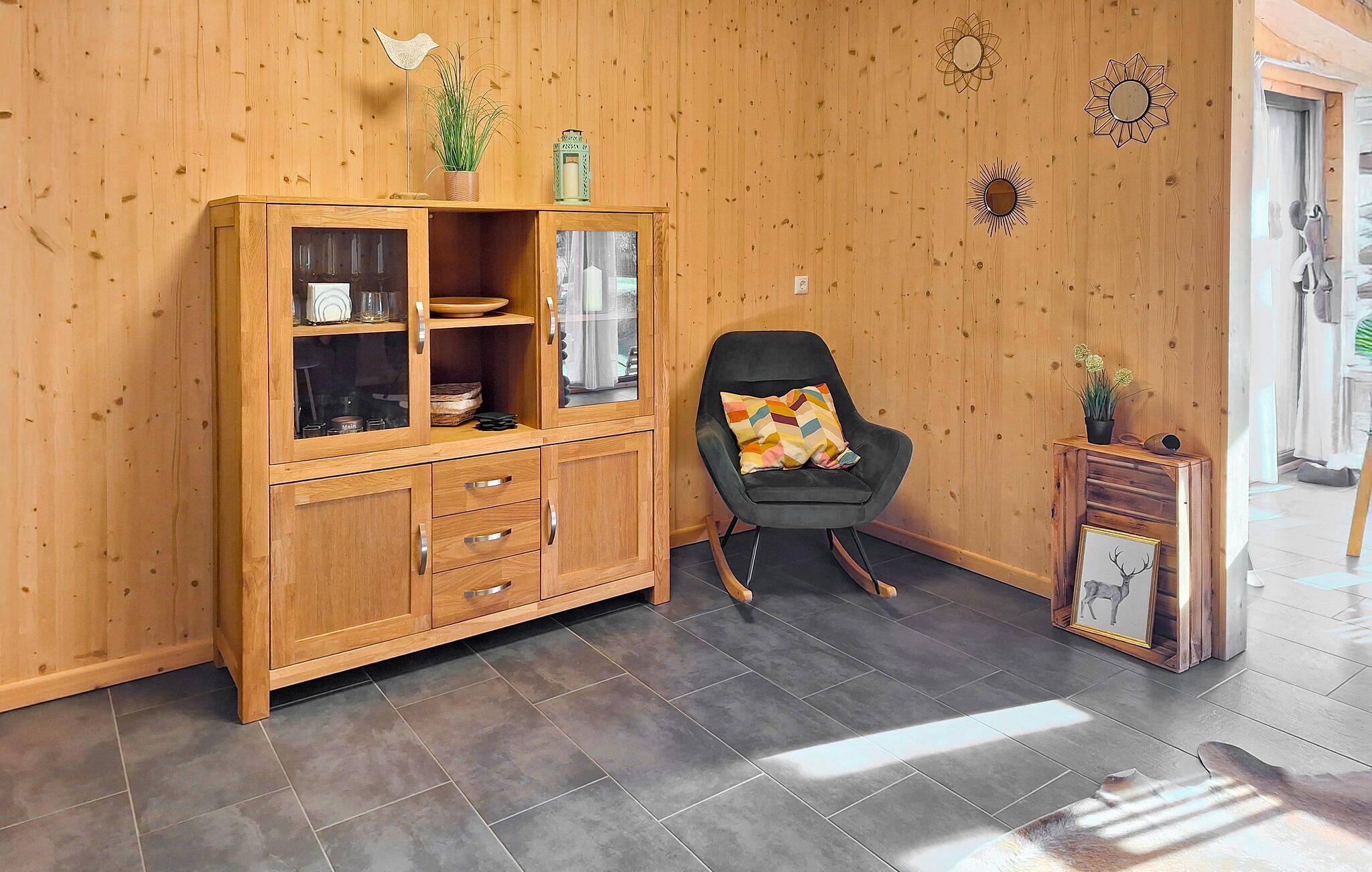 A wooden cabinet with glass doors, a black chair with a colorful cushion, and a small table with a framed picture.