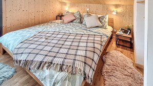 A bedroom with a wooden ceiling, a bed with a patterned blanket, pillows, a nightstand with a tablet, and a fluffy rug. - 3 bedroom pet friendly home in Hohentauern (Hohentauern)