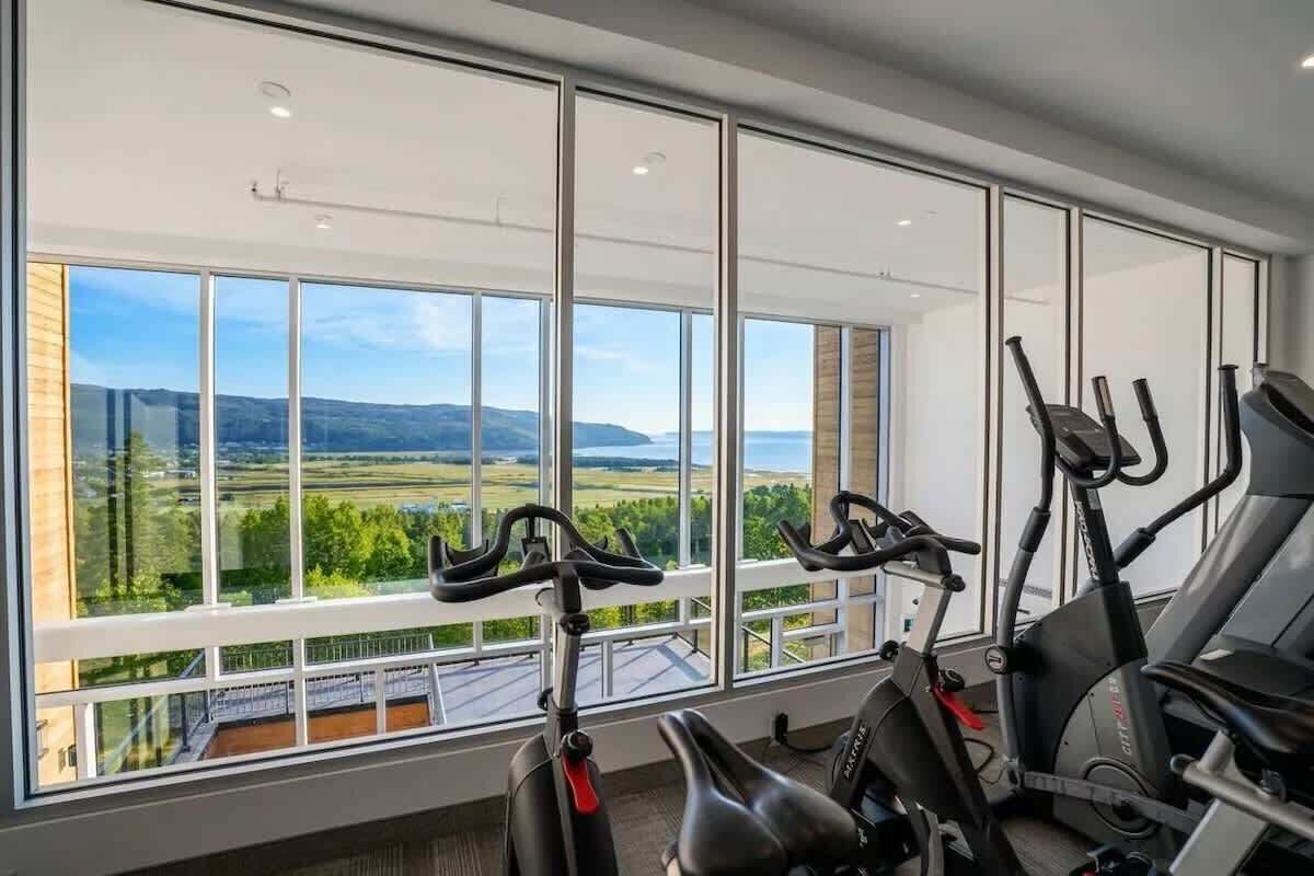 Une salle de sport dotée de grandes fenêtres et d’appareils d’exercice.