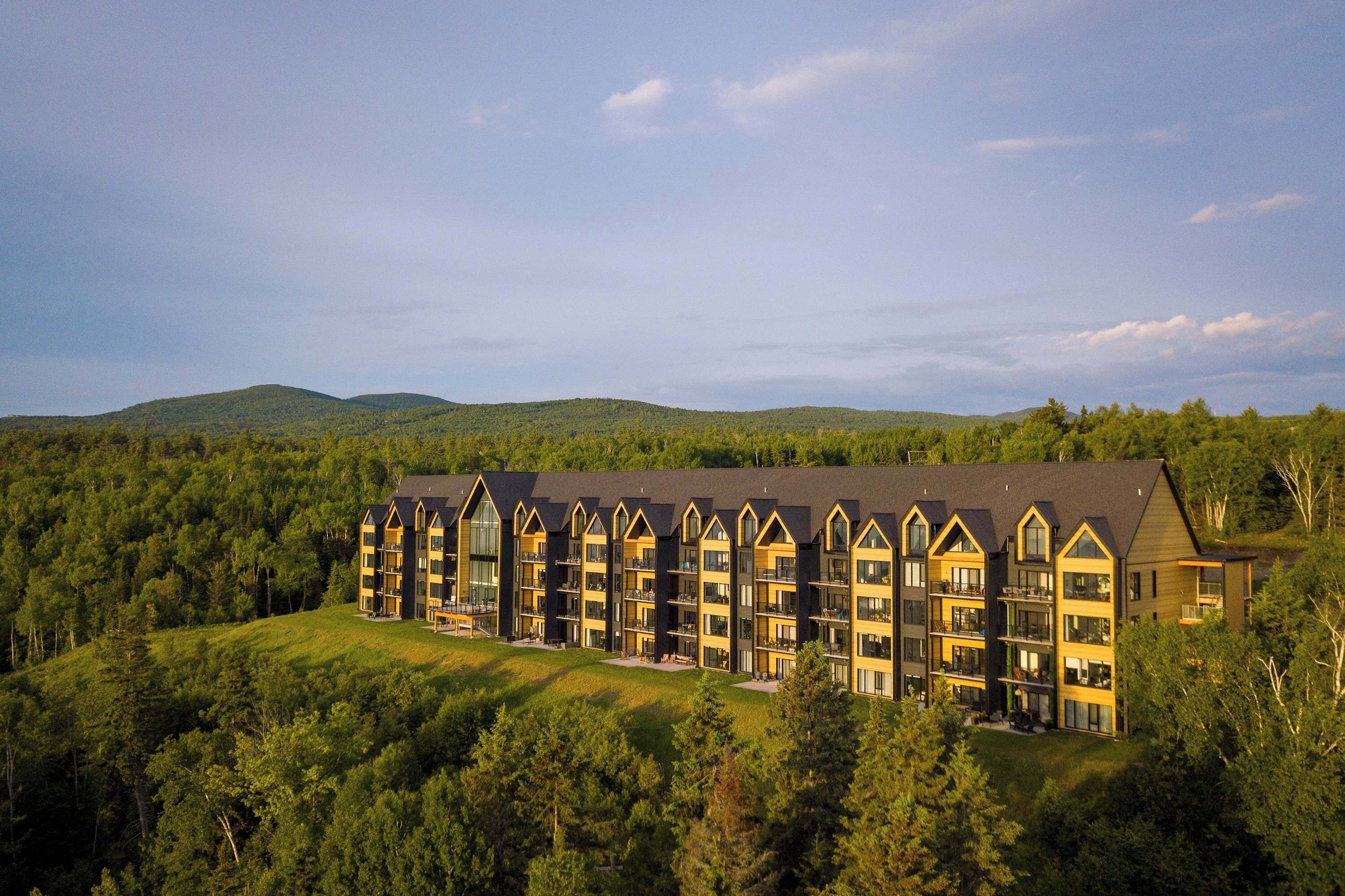 A multi-story hotel with a modern architectural design, situated on a hillside surrounded by dense forest.