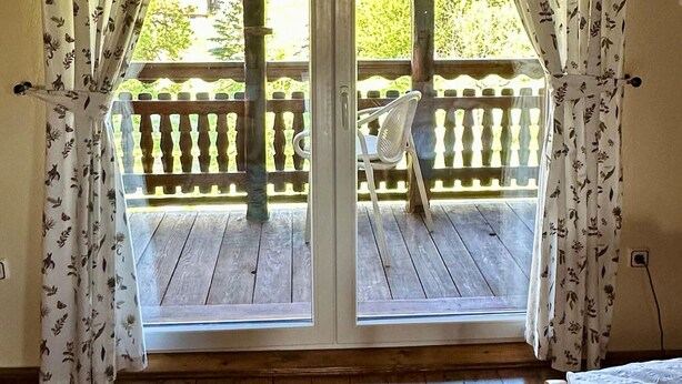 A room with a wooden floor, a white bed, and a view of an outdoor balcony with a wooden railing and a chair. - 1 bedroom cozy home in Duga Resa (Duga Resa)