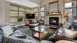 A spacious living room with a fireplace, leather sofas, a television, and large windows. - Mountain-View 3BR | Near Gondola + Pool & Kitchen (Keystone)