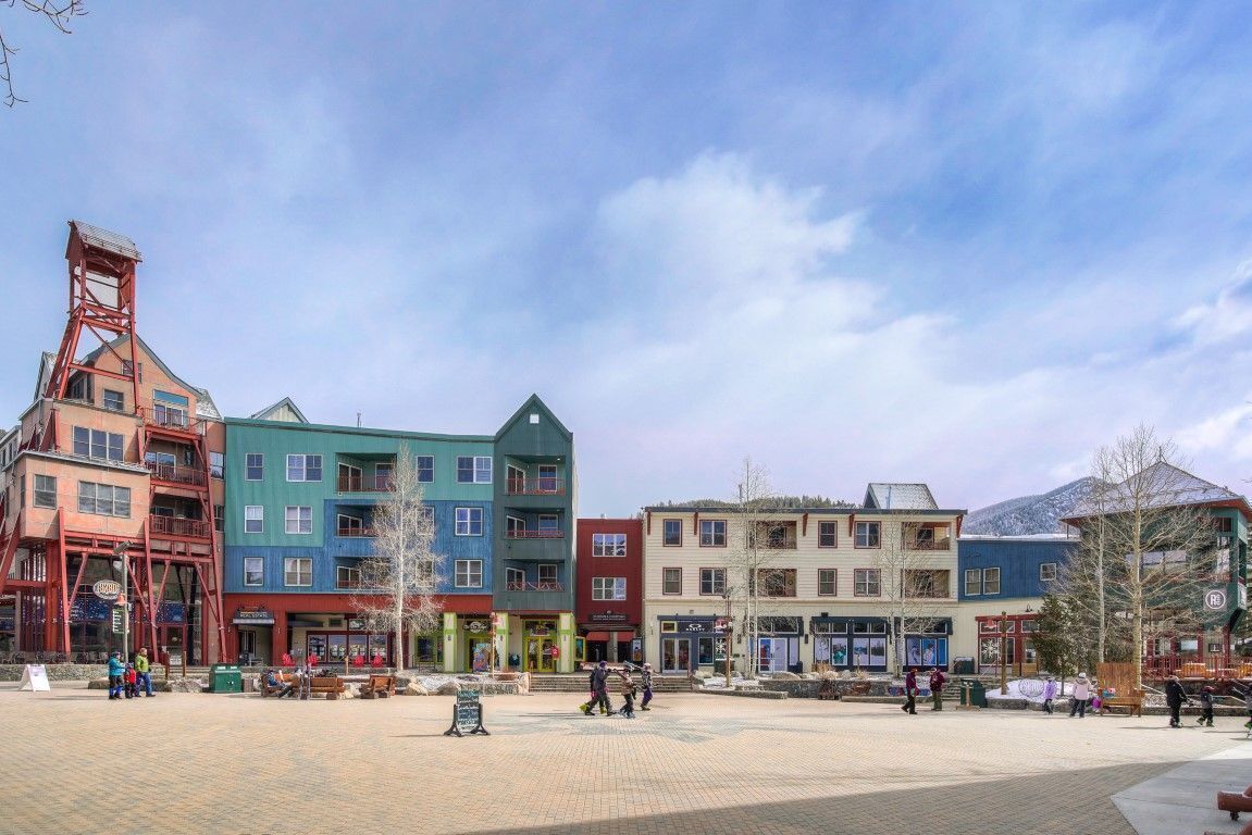 A square with colorful buildings, a prominent red tower, and a clear sky.