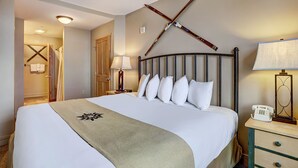 Hotellihuone, jossa on suuri sänky, puinen pääty, yöpöytä lampun kanssa ja puhelin.