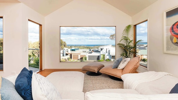 A modern living room with a large window offering a view of residential buildings and a clear sky. - Sweeping Ocean Views (Torquay)