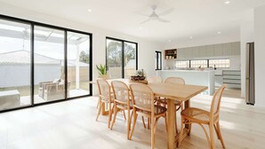 Ein geräumiger Essbereich mit Holztisch und Stühlen, große Schiebeglasfenster, die zum Garten führen, und eine moderne Küche im Hintergrund.