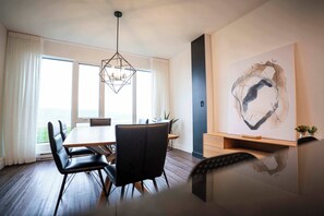 Un espace repas moderne avec une table en bois et des chaises noires, un luminaire suspendu aux formes géométriques et un grand tableau abstrait accroché au mur.