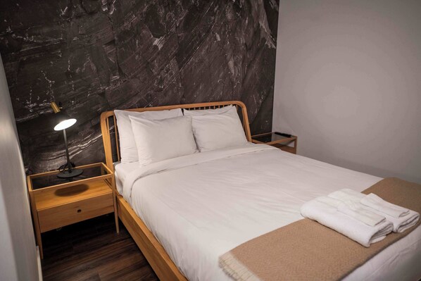 A neatly made bed with white linens, a wooden headboard, and a bedside lamp. - 103 | Bright Condo | Pool and Stunning View (Baie-Saint-Paul)