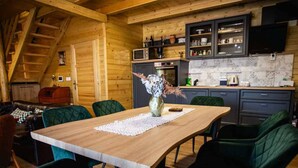 Un interior acogedor de madera con una mesa de comedor, sillas, un sofá y una zona de cocina con armarios y electrodomésticos.
