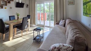 A living room with a sofa, a dining table with chairs, a TV mounted on the wall, and a large window with a view of greenery outside. - Cozy apartment in Orebic with WiFi (Orebic)