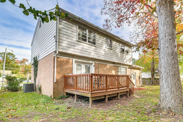 A two-story house with a wooden deck, brick foundation, and a large tree in the yard. - Near Beaches, Base & Bay! Hampton Home w/ Backyard (Hampton)
