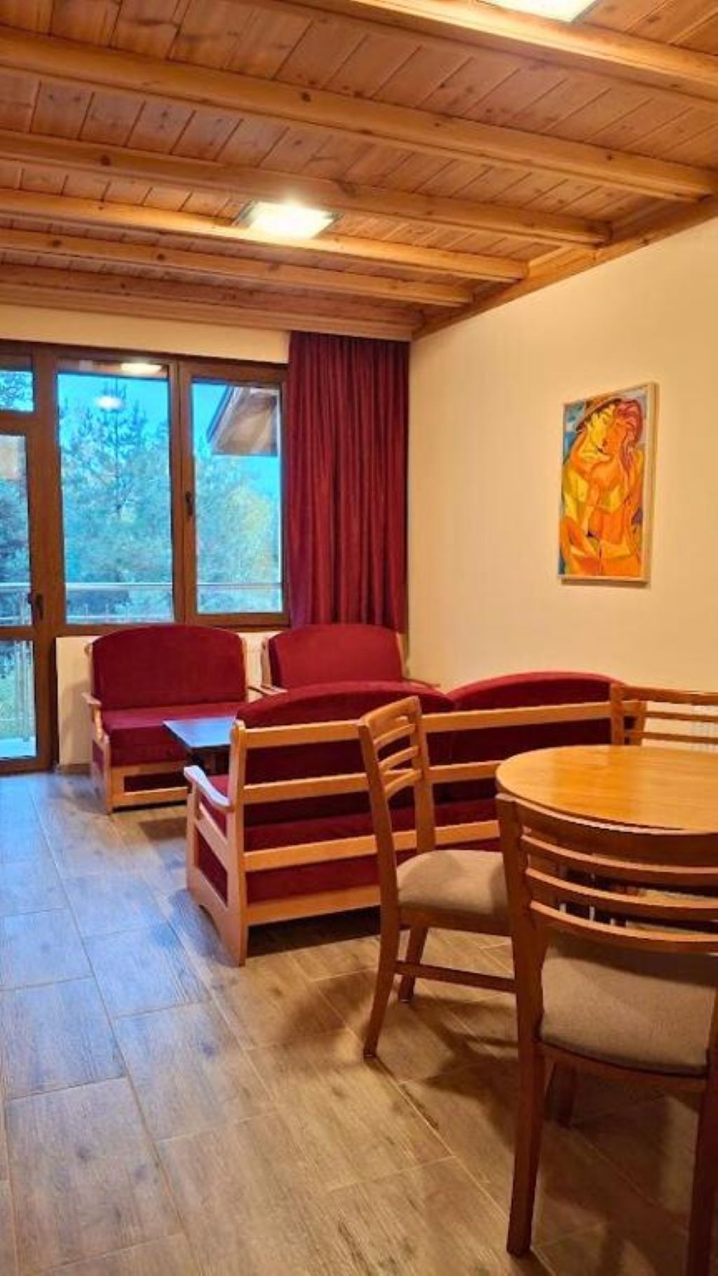 Een gezellige kamer met een houten plafond, een rode bank, een houten eettafel en een schilderij aan de muur.
