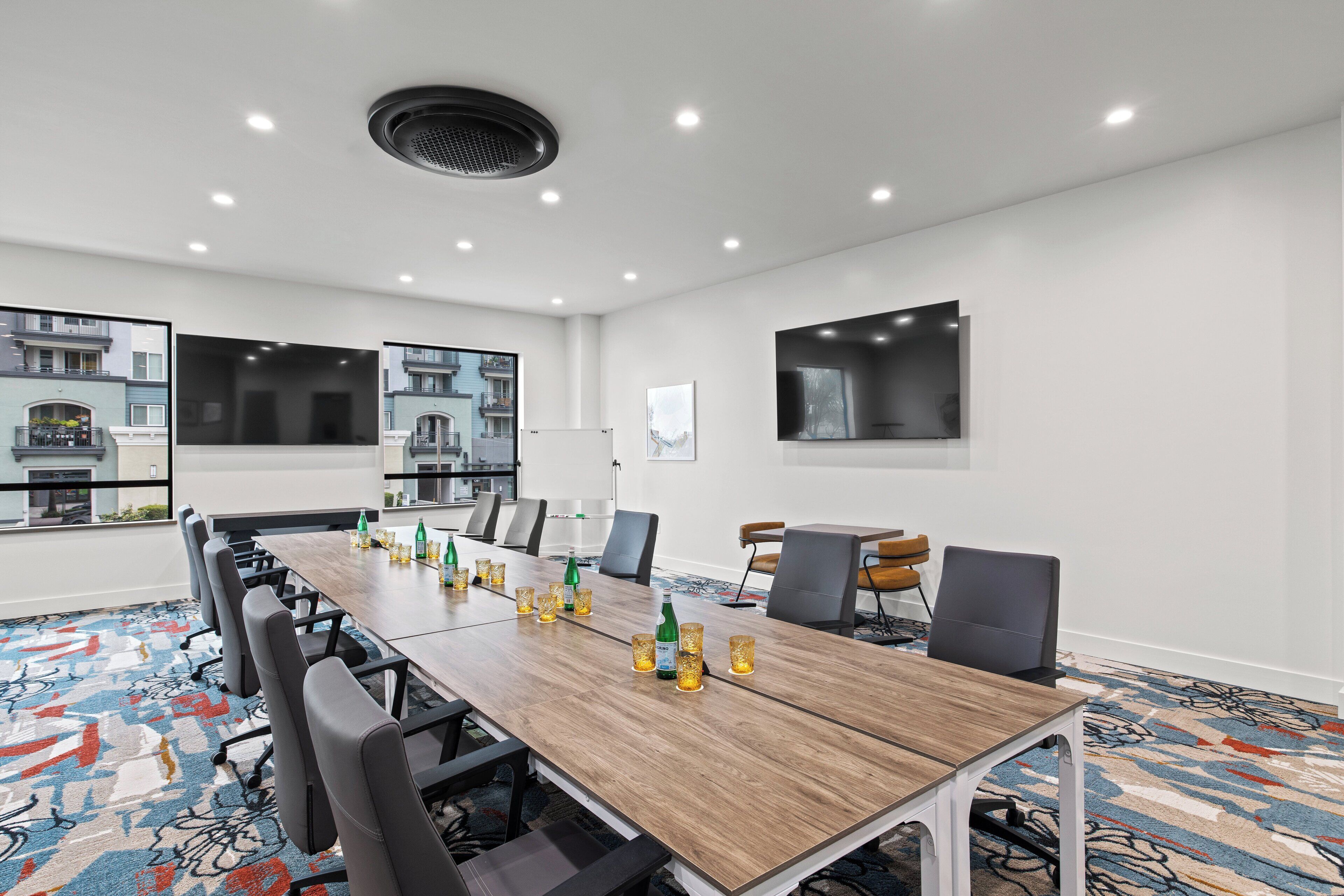 A conference room with a long table, chairs, and a large screen.