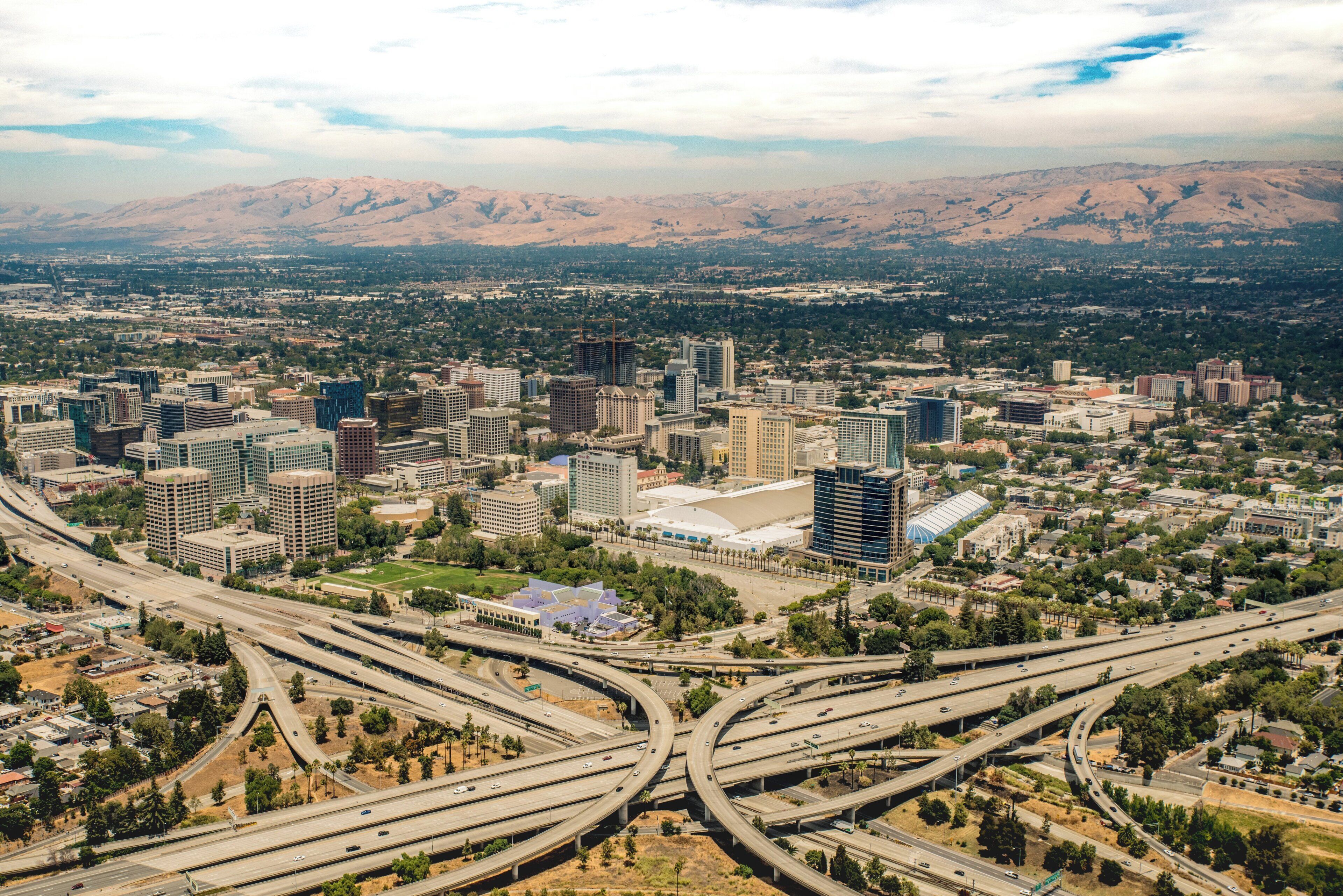 An aerial view of a city with multiple highways, buildings, and mountains in the background.