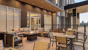 An outdoor seating area with sofas, chairs, and a table, featuring a modern design with wooden elements and glass partitions.
