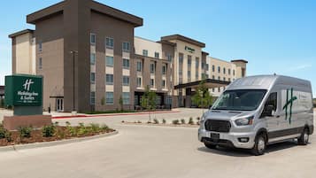 A Holiday Inn & Suites building with a modern design, featuring a large parking area and a delivery van in front.