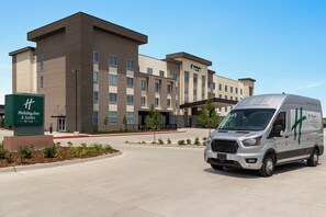 A Holiday Inn & Suites building with a modern design, featuring a large parking area and a delivery van in front. - Holiday Inn Hotel And Suites Commerce City Denver Airport By Ihg (Commerce City)