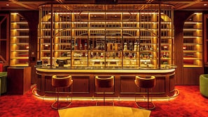 A bar area with a curved counter, multiple shelves of bottles, and three bar stools. - voco Dubai Nice The Heart of Europe by IHG (Dubai)