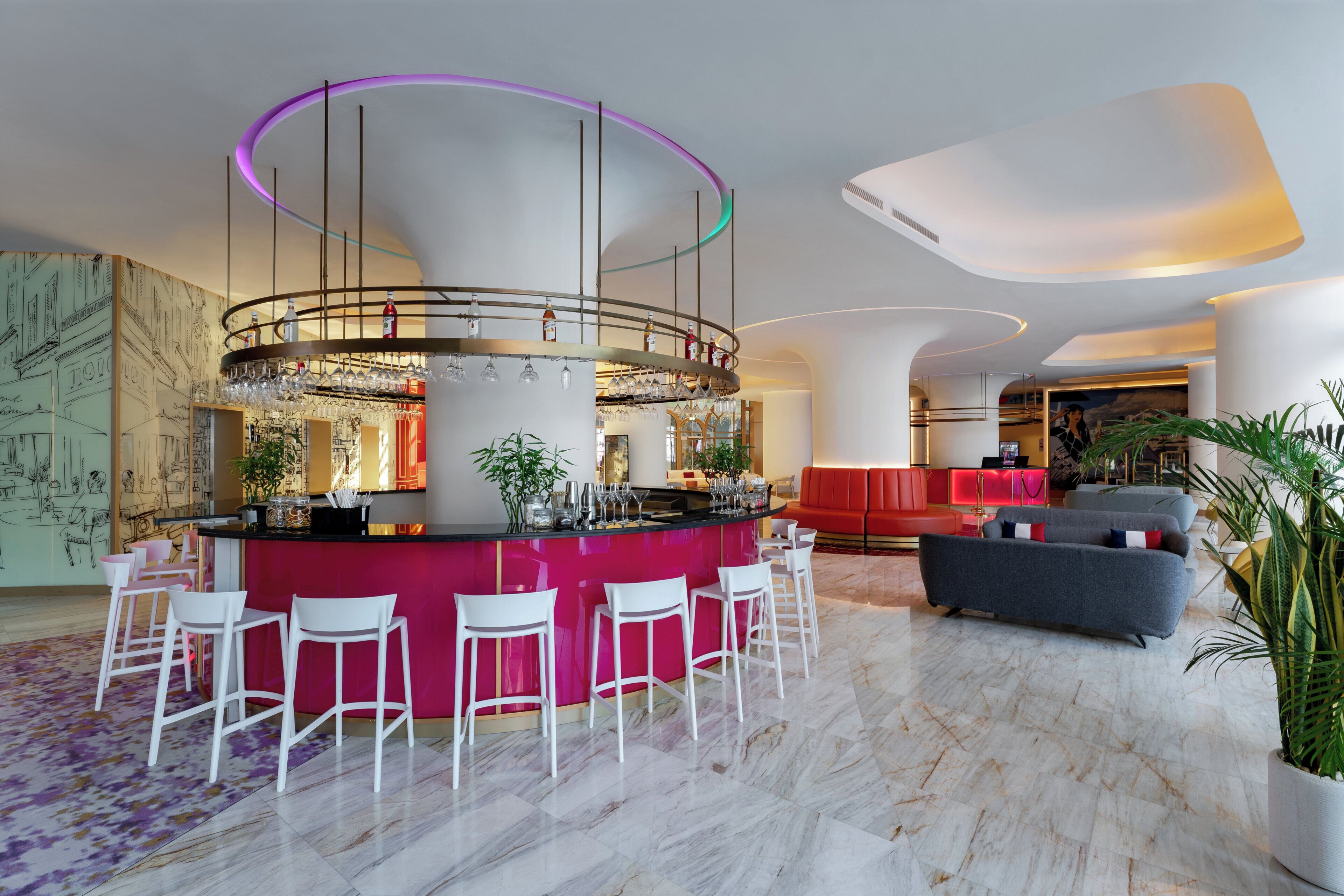A modern bar area with a central bar, white bar stools, and a vibrant red accent wall.