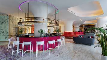 A modern bar area with a central bar, white bar stools, and a vibrant red accent wall.