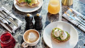 Una mesa con desayuno que incluye un sándwich, un vaso de jugo de naranja, una taza de café y un plato con un huevo escalfado sobre tostada.