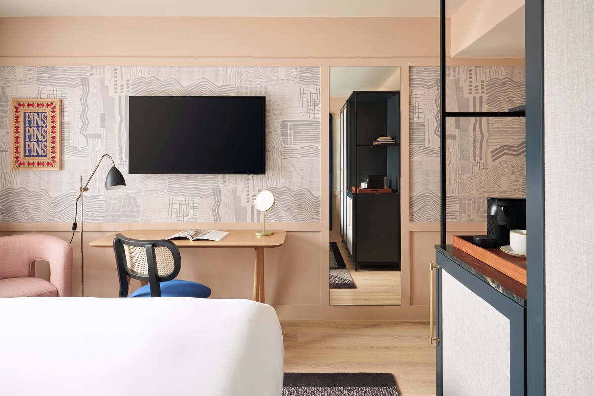 Una habitación de hotel moderna con cama, escritorio, silla y un espejo grande.