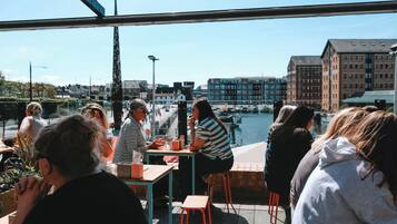 A group of people seated at tables on an outdoor patio with a view of a canal and buildings in the background.
