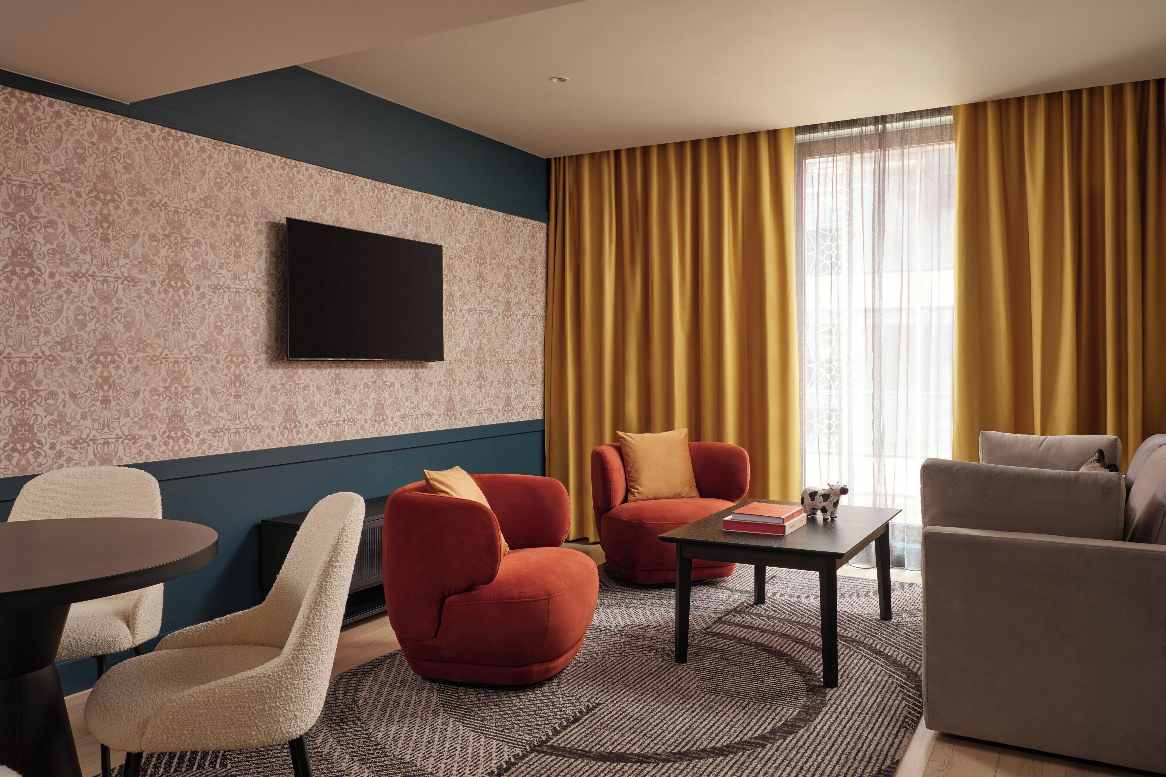 A modern hotel room with a flat-screen TV, two sofas, a round table, and a patterned rug.