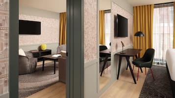 A modern hotel room with a sofa, a dining table, a TV, and a desk with a chair.