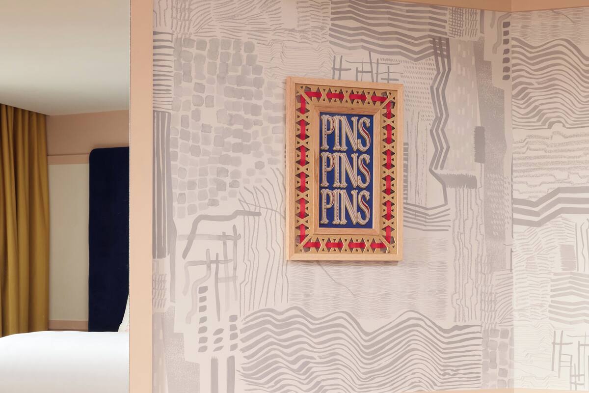 Una pared con un diseño geométrico y un letrero enmarcado que dice 'PINS PINS PINS'.