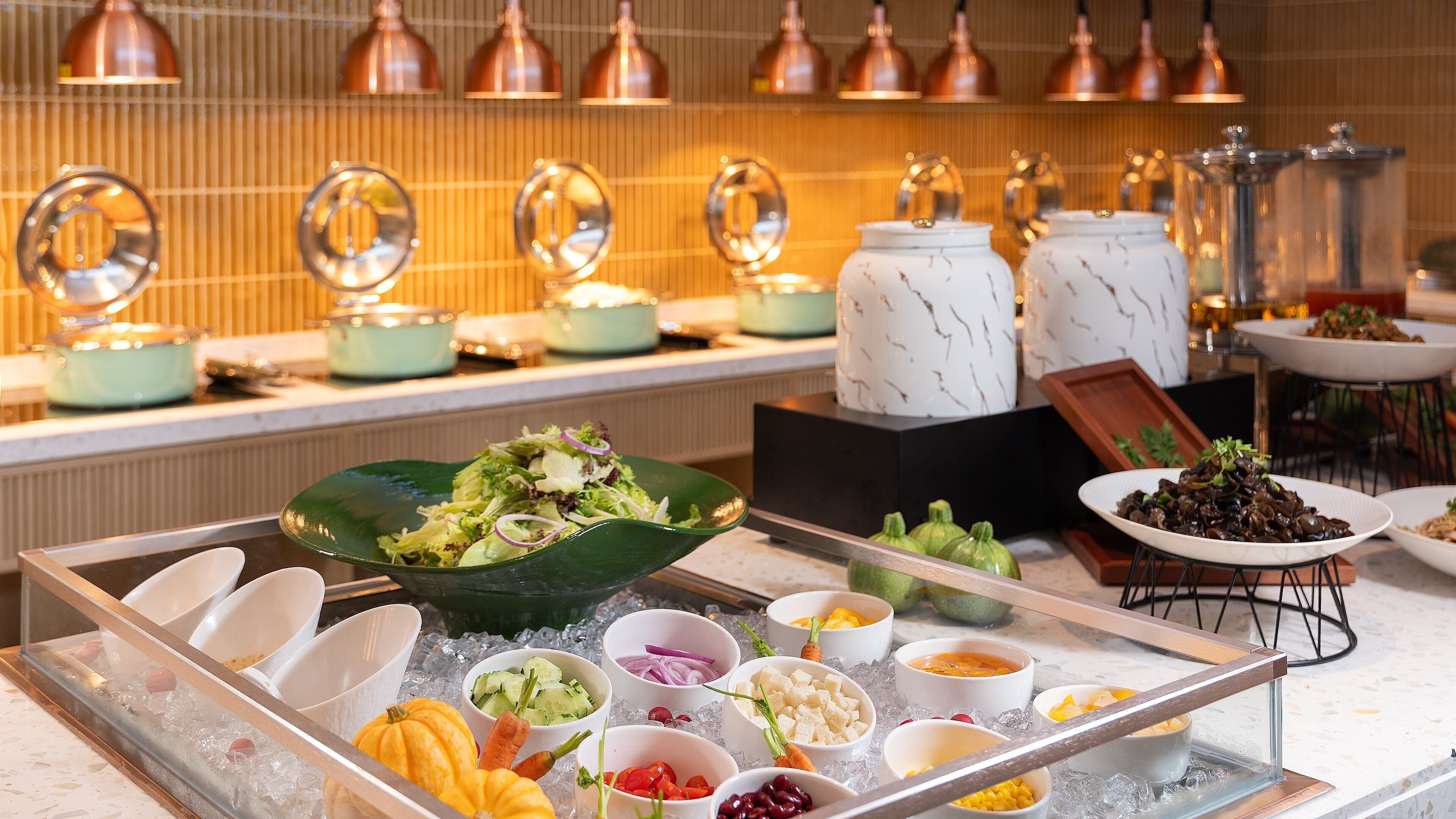 A buffet with various food items and bowls on ice, a marble countertop, and copper pendant lights.