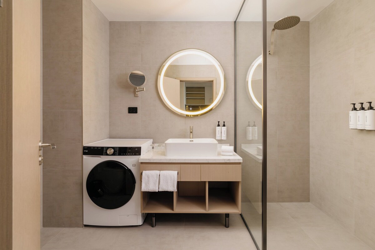 A modern bathroom with a washing machine, a sink, a mirror, and a shower.