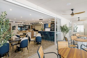 A modern dining area with a herringbone floor, wooden tables, and blue chairs. - voco Darwin Suites by IHG (Darwin)