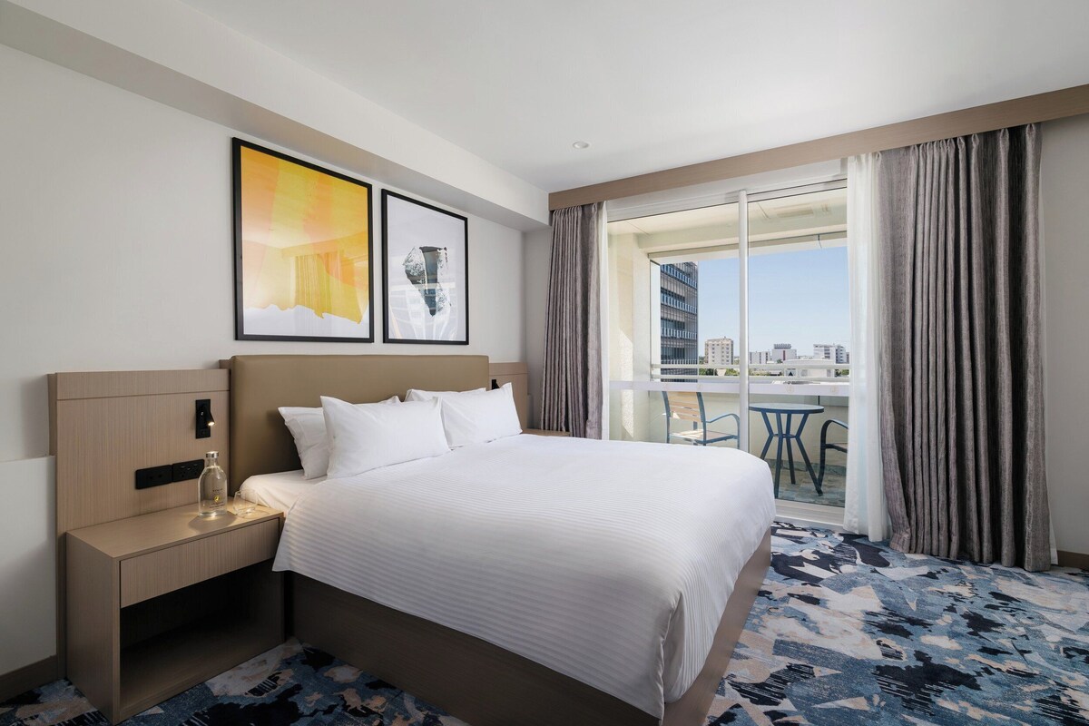 A hotel room with a bed, a nightstand, a glass bottle, and two framed pictures on the wall.