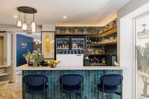 A bar area with a counter, three blue chairs, a refrigerator stocked with bottles, and a decorative bird on the shelf. - voco Darwin Suites by IHG (Darwin)