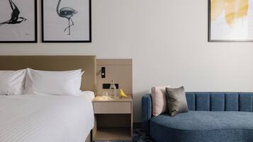 A hotel room with a bed, a nightstand, a blue sofa, and two framed wall art pieces.