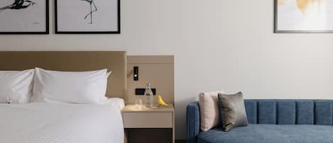 A hotel room with a bed, a nightstand, a blue sofa, and two framed wall art pieces.