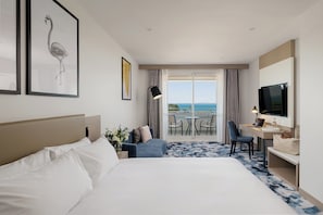 A hotel room with a bed, a desk with a TV, a chair, a small table, a lamp, and a balcony with a view. - voco Darwin Suites by IHG (Darwin)