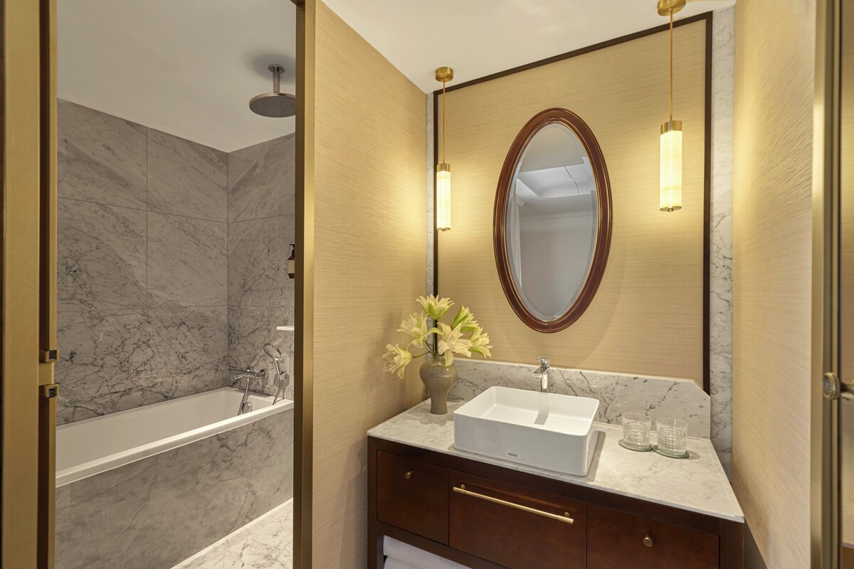 A bathroom with a bathtub, a sink, a mirror, and a vase with flowers.
