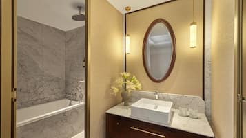 Un baño con bañera, lavamanos, espejo y un florero con flores.