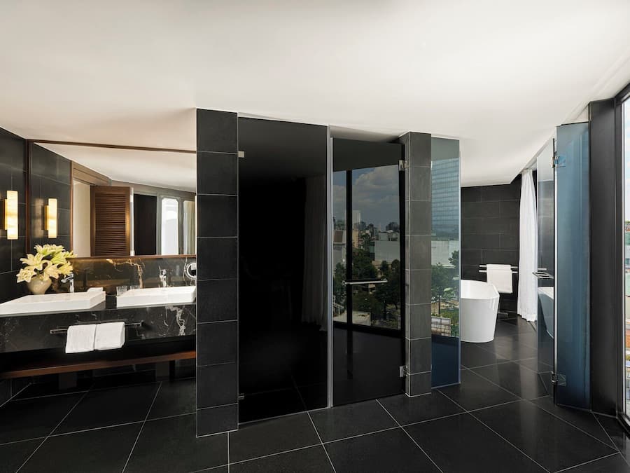 A modern bathroom with a dual sink vanity, a large mirror, and a view of the city through a glass door.