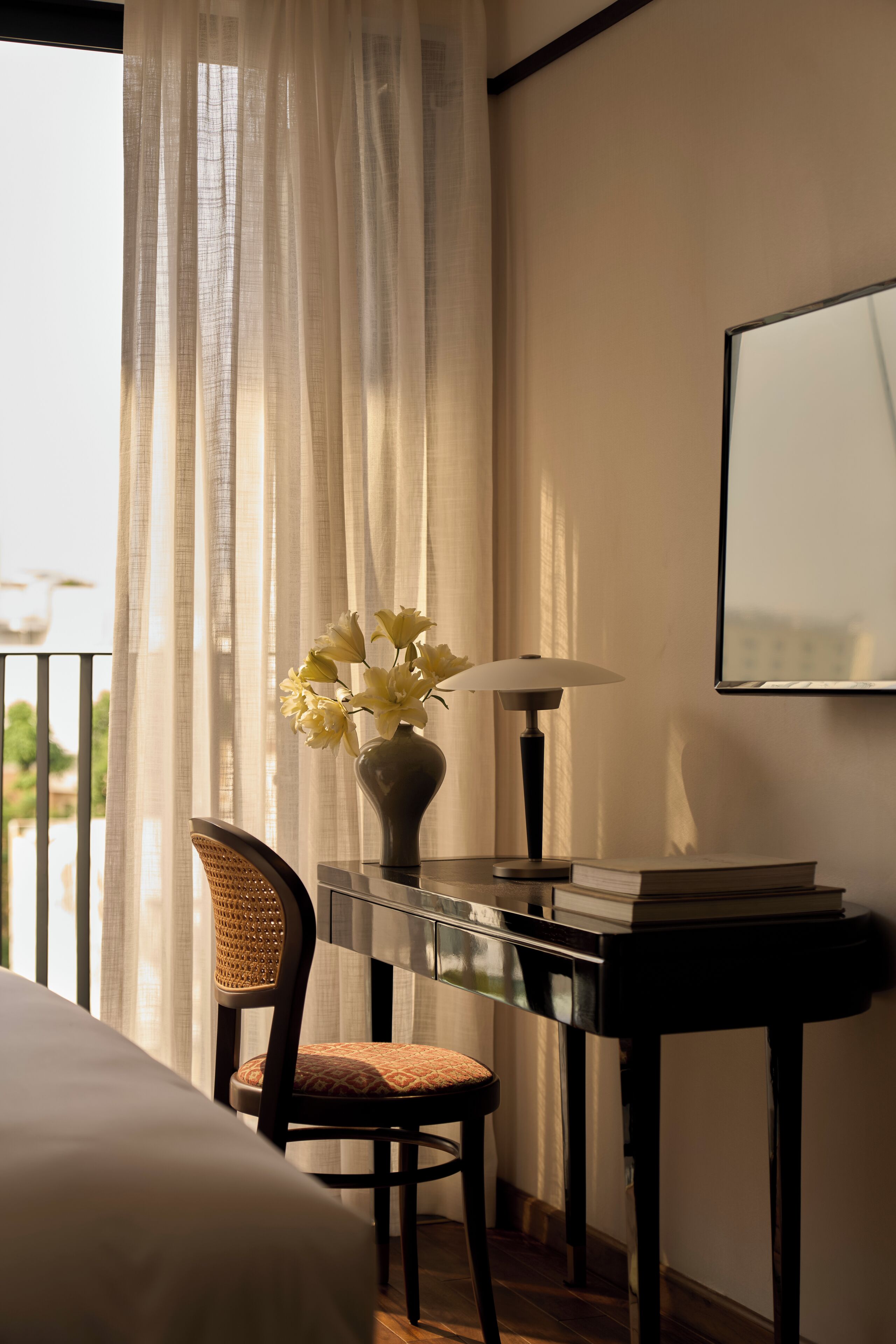A hotel room with a bed, a desk with a lamp, a chair, and a vase with flowers.